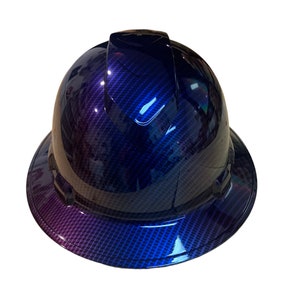 Könnte beinhalten: Ein Helm mit einem blauen und violetten Karbonfaser-Muster. Der Helm hat einen schwarzen Rand und eine schwarze Oberseite.