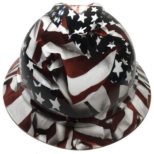Puede incluir: Un casco de obra con un dise&ntilde;o de bandera americana blanca, roja y azul. La bandera se representa como si estuviera ondeando y flotando en el viento.