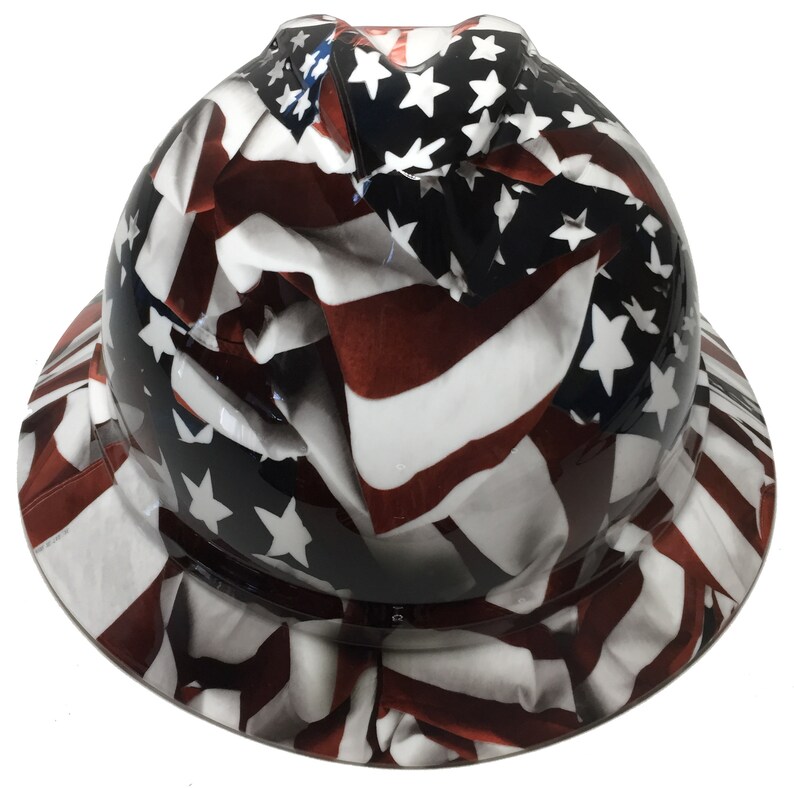 Puede incluir: Un casco de obra con un dise&ntilde;o de bandera americana blanca, roja y azul. La bandera se representa como si estuviera ondeando y flotando en el viento.