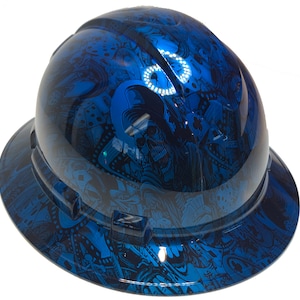 Könnte beinhalten: Ein blauer Schutzhelm mit einem Totenkopf- und Würfelmuster. Der Helm hat einen breiten Rand und einen schwarzen Riemen.