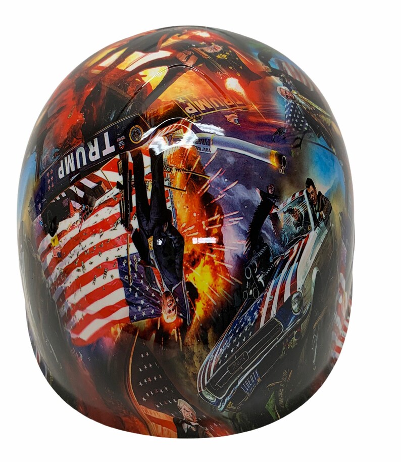 May include: A hard hat with a colorful collage design featuring an American flag, a car, and a man in a suit. The design also includes the word "TRUMP" and the text "LIBERTY".