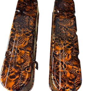 May include: A pair of orange and black skull-patterned valve covers. The covers are made of metal and have a glossy finish.