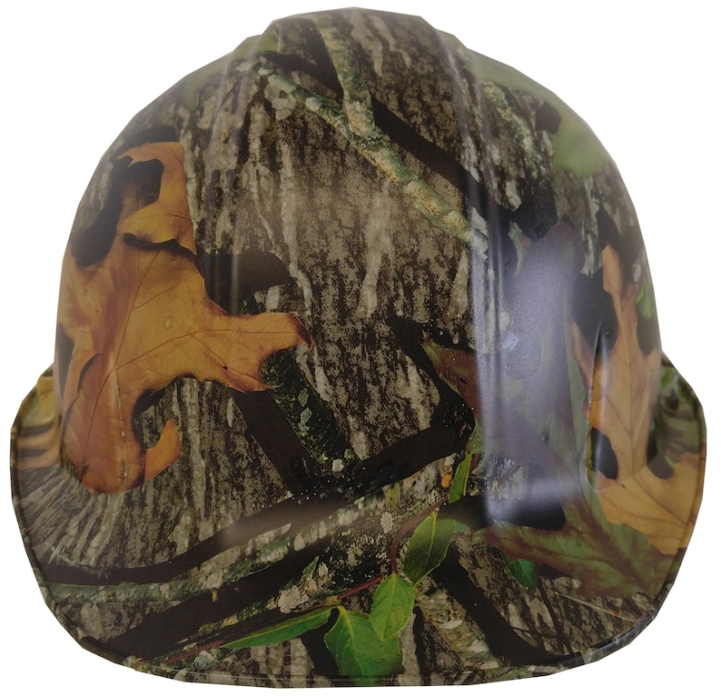 May include: A camouflage hard hat with a brown, green and white pattern. The hat has a wide brim and a smooth surface.