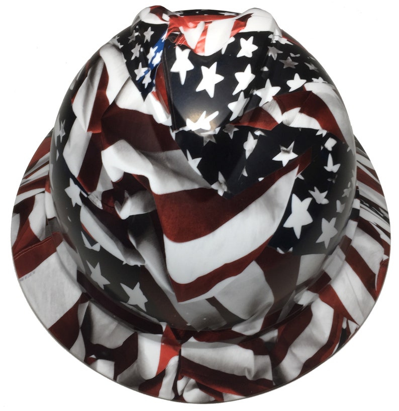 Puede incluir: Un casco de obra con un gr&aacute;fico de la bandera estadounidense. La bandera est&aacute; impresa en rojo, blanco y azul con estrellas y rayas.