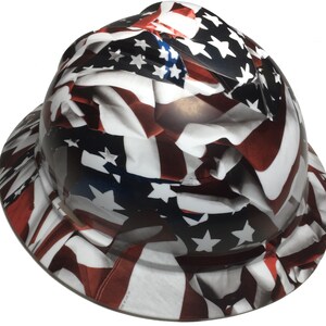 Puede incluir: Un casco blanco con un dise&ntilde;o de bandera americana roja, blanca y azul. La bandera est&aacute; impresa en toda la superficie del casco.