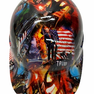May include: A hard hat with a colorful design featuring images of Donald Trump, American flags, and patriotic imagery. The text "TRUMP" is visible on the hat.