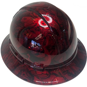 Könnte beinhalten: Ein roter Schutzhelm mit einem schwarzen und roten grafischen Design. Das Design zeigt einen Schädel und andere abstrakte Formen.