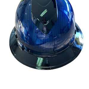 Puede incluir: Un casco azul con un patrón de fibra de carbono negro y una parte superior negra. El casco tiene una visera negra.
