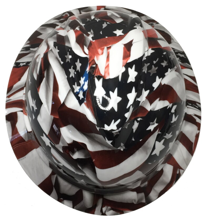 Puede incluir: Un casco de seguridad con un dise&ntilde;o de bandera estadounidense blanca, roja y azul. La bandera est&aacute; drapeada sobre el casco y parece ondear al viento.