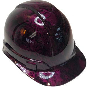 Könnte beinhalten: Ein lilafarbener Schutzhelm mit einem schwarzen und weißen abstrakten Muster. Der Helm hat einen Schirm und einen Kinnriemen.