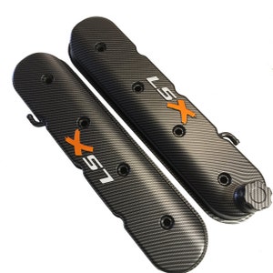 Könnte beinhalten: Ein Paar schwarze Ventildeckel aus Carbonfaser mit einem weißen "LSX"-Logo und orangefarbenen Akzenten.