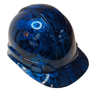 Könnte beinhalten: Ein blauer Schutzhelm mit einem schwarz-weißen grafischen Design. Das Design zeigt einen Schädel, Würfel und andere abstrakte Muster.