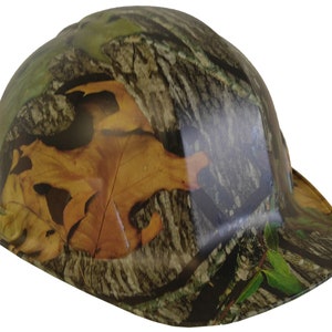 May include: A hard hat with a camouflage pattern featuring brown, green, and tan colours. The pattern includes leaves and tree bark.