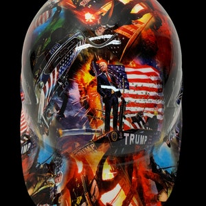 May include: A white hard hat with a colorful graphic design featuring an American flag, a portrait of Donald Trump, and other patriotic imagery. The text "TRUMP" is visible on the hat.