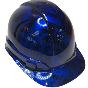 Könnte beinhalten: Ein blauer Schutzhelm mit einem Totenkopf- und Würfel-Grafikdesign. Der Helm hat einen schwarzen Rand und einen weißen reflektierenden Streifen am Rand.