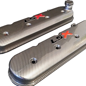 May include: A pair of black and silver engine valve covers with a carbon fiber pattern and the text "LSX" in black with a red "X".