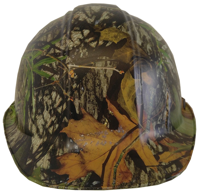 May include: A hard hat with a camouflage pattern featuring brown, green, and tan leaves and branches.