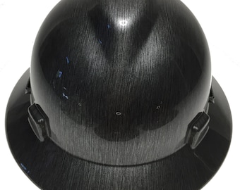 May include: A black hard hat with a wood grain pattern. The hat has a brim and a chin strap.