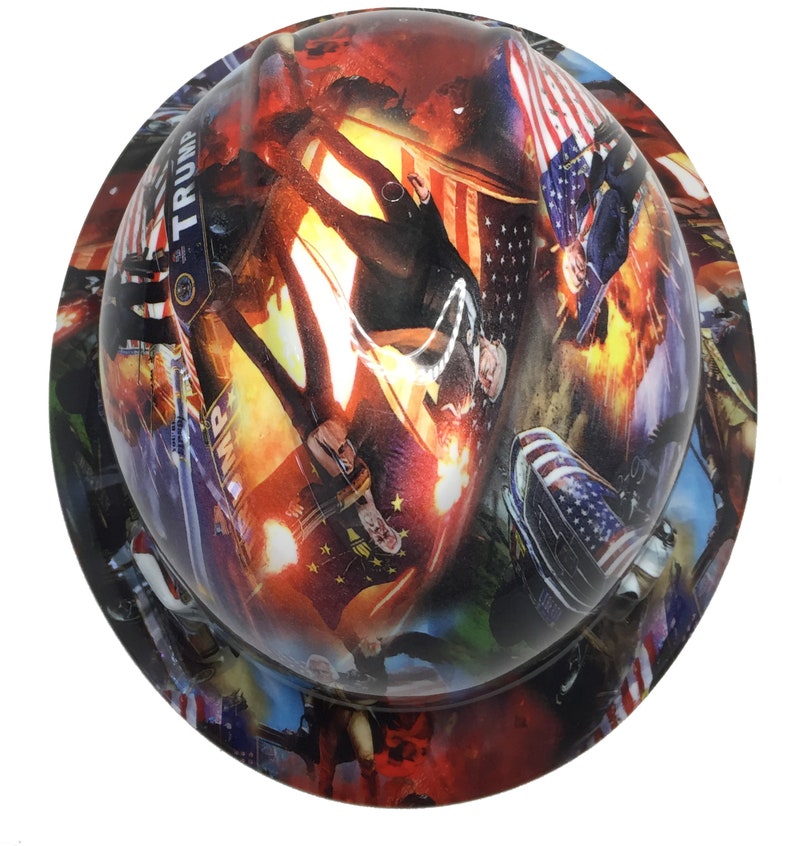 May include: A hard hat with a colorful, digitally printed design. The design features images of people, flags, and the word "TRUMP". The overall color scheme includes red, white, blue, and orange.