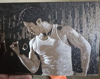 May include: A rectangular wall art piece featuring a textured, metallic bronze and silver relief of a person wearing a tank top. The figure is set against a dark, black background with vertical, etched lines that create a high-contrast, industrial aesthetic.