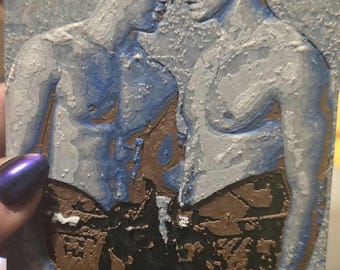 May include: A rectangular art piece featuring a textured, relief-style depiction of two figures standing face-to-face. The figures are rendered in shades of blue, brown, and white, with dark brown shorts and blue and white leg coverings.