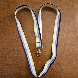 May include: A lanyard with a yellow, white, purple, and black striped pattern. The lanyard has a silver clip attached to it.