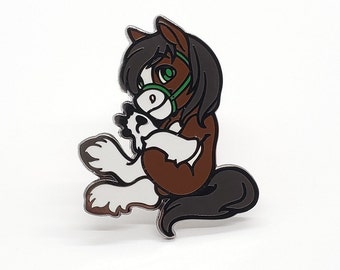 May include: A brown and white horse with a green bridle, sitting on its haunches with its head turned to the side. The horse is a cartoon-style enamel pin.