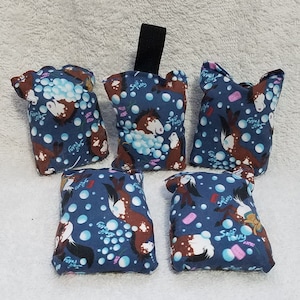 Puede incluir: Cinco bolsas de tela azul con un patrón de caballo y burbujas. Las bolsas están llenas de frijoles o arroz y tienen un lazo para colgar. Las bolsas están etiquetadas como "Soap Pony".
