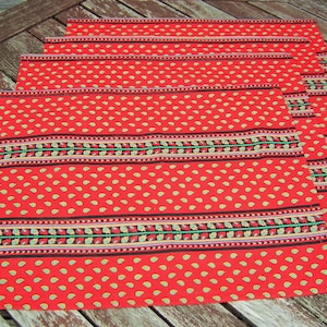 May include: Set of four red placemats with a paisley pattern and a black, white, and green border. The placemats are made of fabric and have a slightly textured surface.