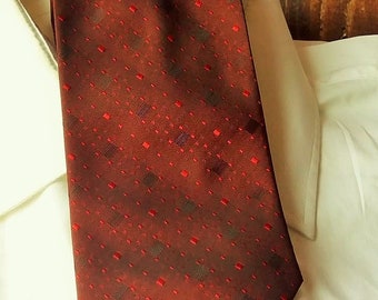 Puede incluir: Una corbata de patrón rojo y marrón con un diseño geométrico. La corbata está hecha de un material sedoso y tiene una punta puntiaguda.
