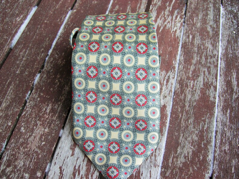May include: A green and yellow patterned tie with red accents. The tie has a repeating pattern of circles and flowers.