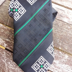 Puede incluir: Corbata negra con un patr&oacute;n geom&eacute;trico verde y blanco. El patr&oacute;n presenta un dise&ntilde;o repetitivo de cuadrados y rombos.