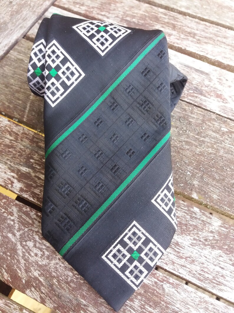 Puede incluir: Corbata negra con un patr&oacute;n geom&eacute;trico verde y blanco. El patr&oacute;n presenta un dise&ntilde;o repetitivo de cuadrados y rombos.