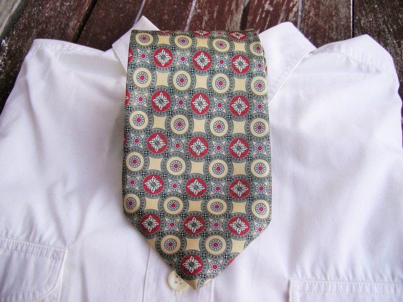 May include: A white dress shirt with a yellow and red patterned tie. The tie has a geometric design with circles and squares.