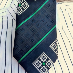 Puede incluir: Una corbata azul oscuro con un patr&oacute;n geom&eacute;trico en blanco y verde. El patr&oacute;n presenta una serie de cuadrados con cuadrados m&aacute;s peque&ntilde;os dentro.