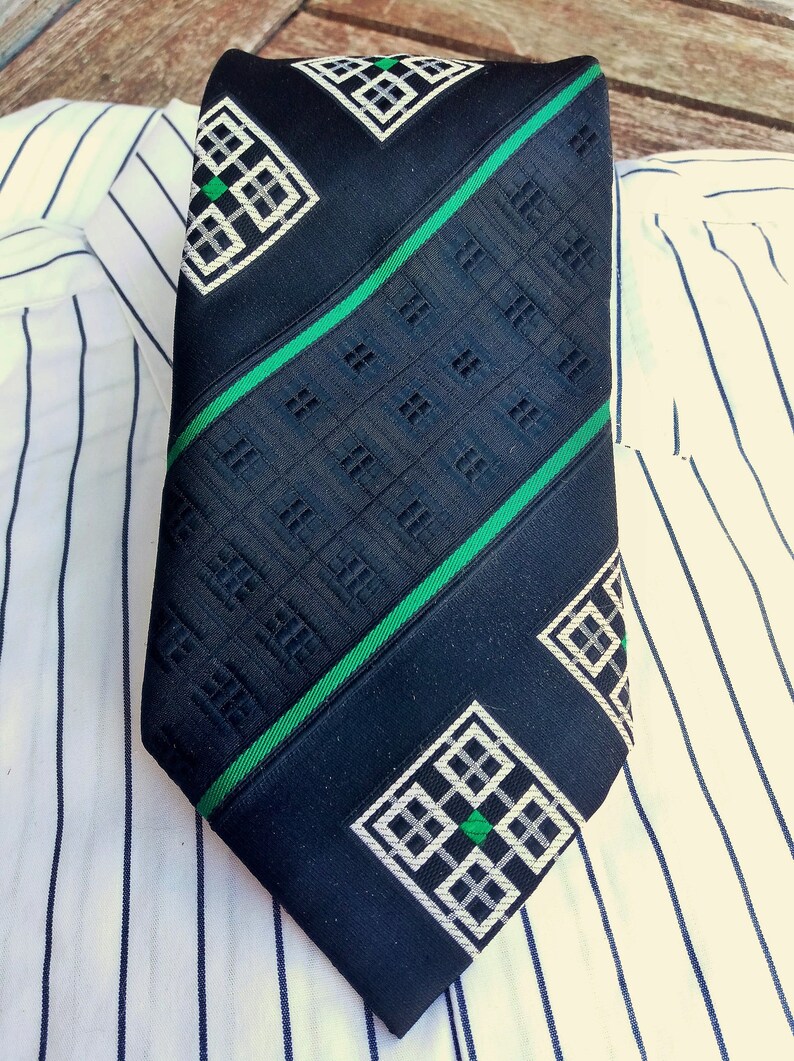 Puede incluir: Una corbata azul oscuro con un patr&oacute;n geom&eacute;trico en blanco y verde. El patr&oacute;n presenta una serie de cuadrados con cuadrados m&aacute;s peque&ntilde;os dentro.