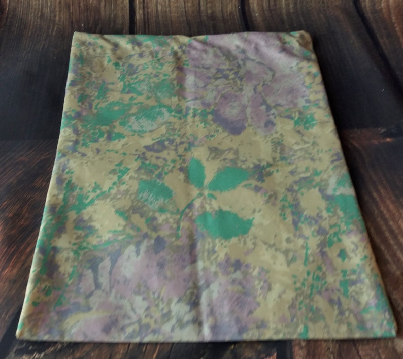 May include: A pillowcase with a floral pattern in shades of green, beige, and purple. The pattern features abstract flowers and leaves.
