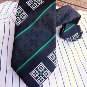 Puede incluir: Una corbata negra y verde con un dise&ntilde;o geom&eacute;trico. La corbata tiene una franja verde que recorre el centro y un patr&oacute;n geom&eacute;trico blanco y negro en los lados.