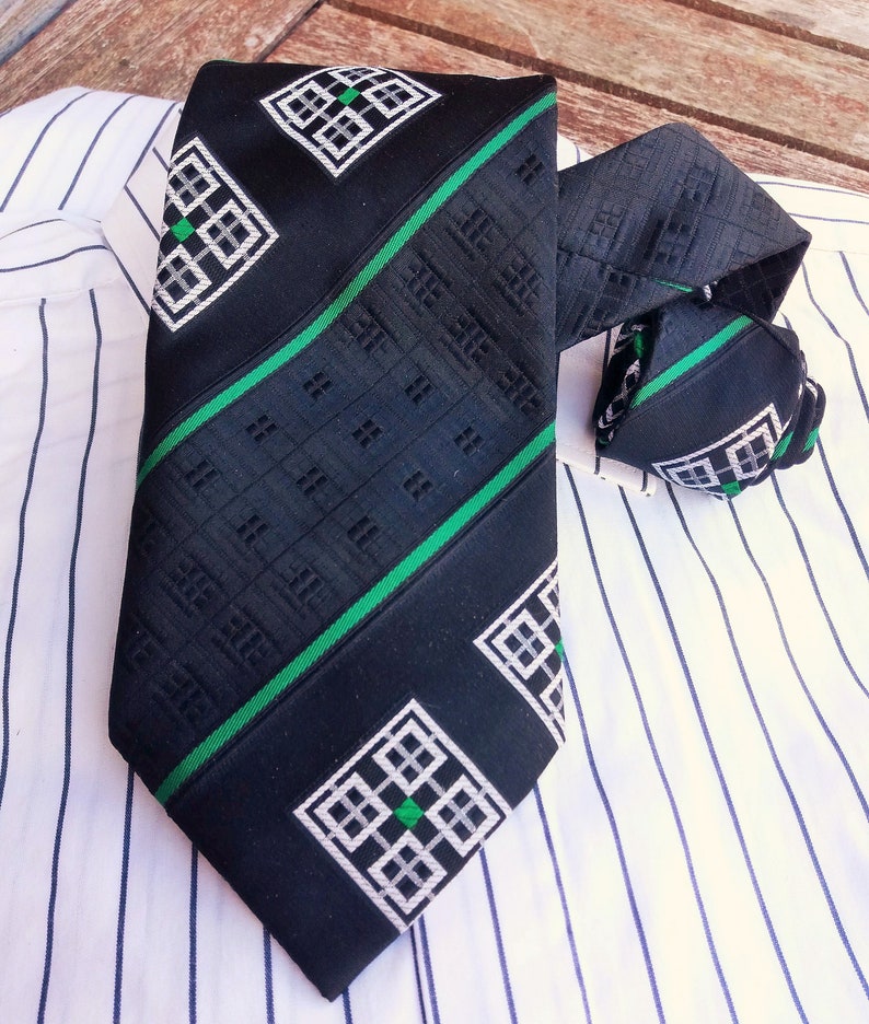 Puede incluir: Una corbata negra y verde con un dise&ntilde;o geom&eacute;trico. La corbata tiene una franja verde que recorre el centro y un patr&oacute;n geom&eacute;trico blanco y negro en los lados.