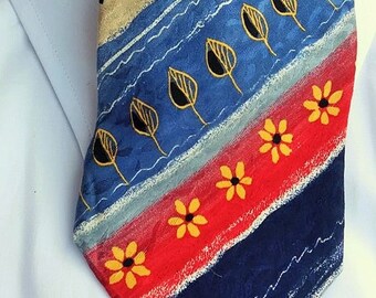 May include: A blue, red, and beige patterned tie with yellow flowers and black leaves. The tie has a diagonal stripe pattern.