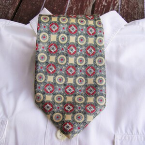May include: A white dress shirt with a patterned tie. The tie has a geometric pattern with red, green, and white circles on a beige background.