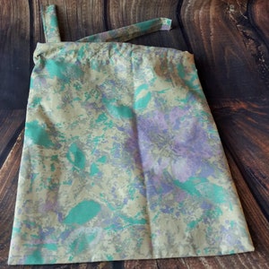 May include: A beige drawstring bag with a green and purple floral pattern.