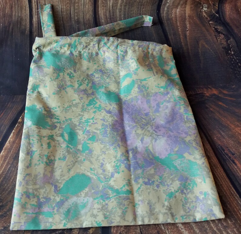 May include: A beige drawstring bag with a green and purple floral pattern.