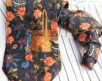 Può includere: Una cravatta di seta blu scuro con un motivo floreale con fiori arancioni, gialli e blu, un cestino e una brocca. La cravatta è su una camicia a righe bianche e blu.