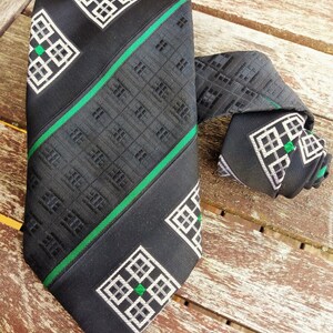 Puede incluir: Una corbata negra con un patr&oacute;n geom&eacute;trico verde y blanco. La corbata tiene un patr&oacute;n repetitivo de cuadrados y rect&aacute;ngulos.