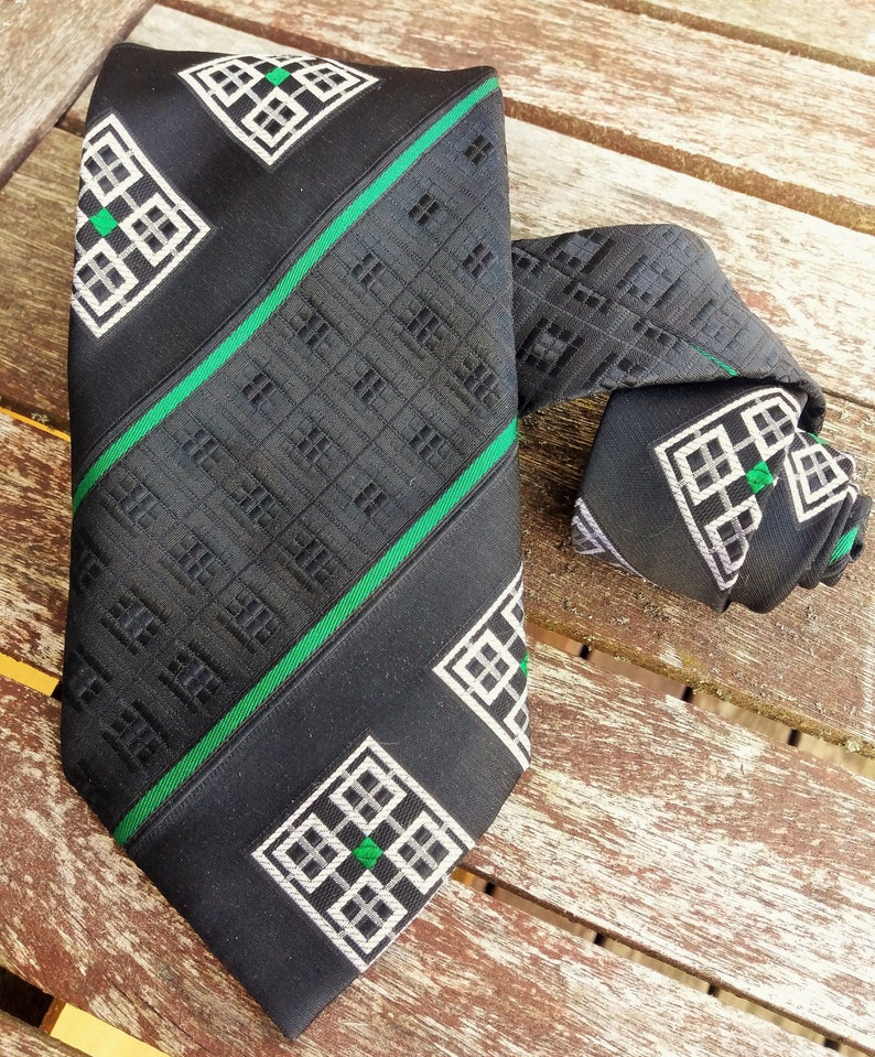 Puede incluir: Una corbata negra con un patr&oacute;n geom&eacute;trico verde y blanco. La corbata tiene un patr&oacute;n repetitivo de cuadrados y rect&aacute;ngulos.