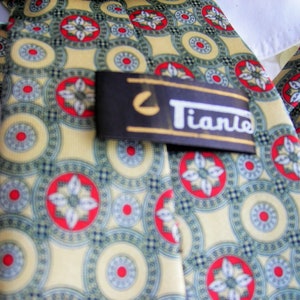 May include: A yellow, green, and red patterned silk tie with a black and white label that reads "Tiano".