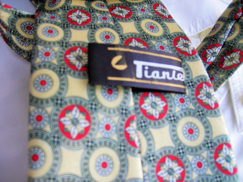 May include: A yellow, green, and red patterned silk tie with a black and white label that reads "Tiano".
