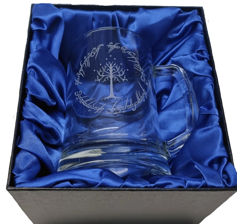 May include: A clear glass mug with a handle, featuring an etched design of the White Tree of Gondor and the inscription "One Ring to rule them all, One Ring to find them, One Ring to bring them all and in the darkness bind them" in Elvish script.