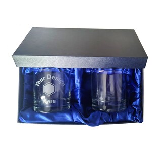 May include: Two clear glass tumblers with a blue satin lining inside a black gift box. One tumbler has the text "Your Design Here" etched on the side.
